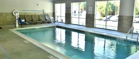 Une piscine intérieure avec des lignes de démarcation bien visibles, un espace vestiaire et de grandes fenêtres offrant une vue sur l’extérieur.