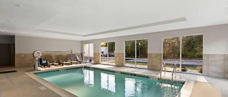 An indoor swimming pool with clear water, a lifeguard chair, and a pool ladder.