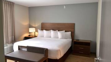 A hotel room with a large bed, a bedside table with a lamp, a chair, and a wooden dresser.