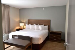 A hotel room with a large bed, a bedside table with a lamp, a chair, and a wooden dresser. - Mainstay Suites Gatlinburg TN (Gatlinburg)