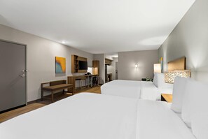 A hotel room with two beds, a desk, a chair, a bench, a TV, and a lamp. - Mainstay Suites Gatlinburg TN (Gatlinburg)