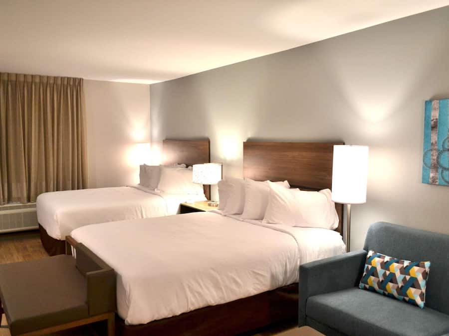 A hotel room with two beds, a sofa, and a wall-mounted artwork.