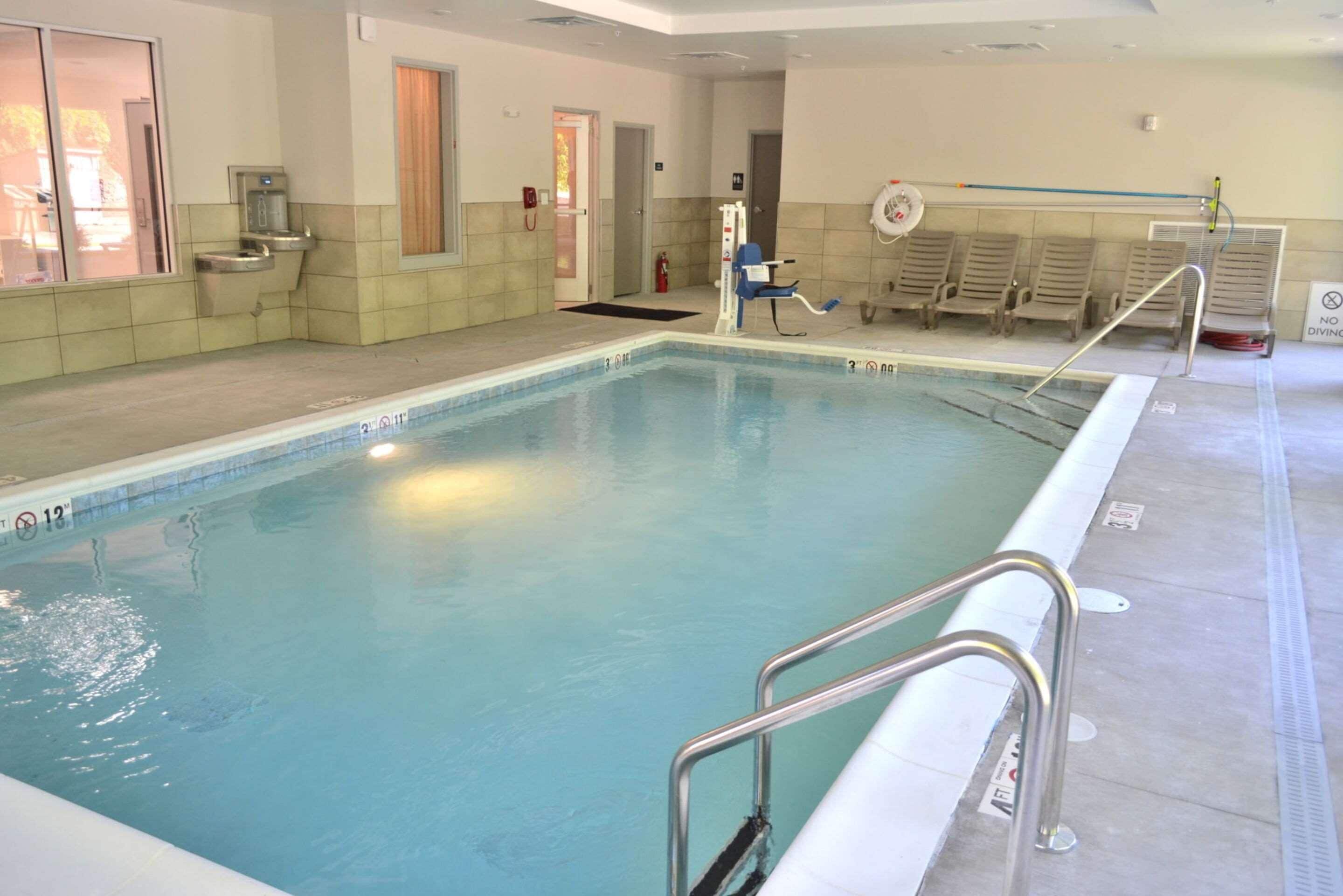 An indoor swimming pool with clear water, a diving board, and a lifeguard chair.