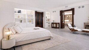 A modern bedroom with a large bed, bedside tables, a vanity with a mirror, and built-in shelving.
