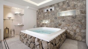 A modern bathroom with a stone wall, a freestanding bathtub, and built-in shelves with candles.