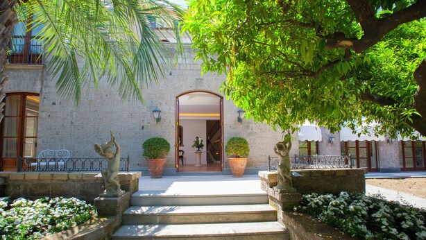 A stone building with a set of steps leading to an arched entrance, surrounded by potted plants and a small garden.