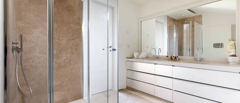 A modern bathroom with a glass-enclosed shower, a white vanity with a large mirror, and a beige tiled floor.