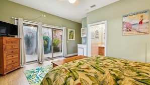 A bedroom with a bed, a wooden dresser, a sliding glass door leading to a balcony, and a poster on the wall. - Welcome to Sunset Sails & Wagging Tails! (St. George Island)