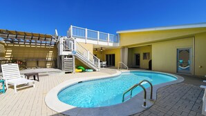 A swimming pool with a small staircase leading to a balcony, surrounded by lounge chairs and a covered area. - Welcome to Sunset Sails & Wagging Tails! (St. George Island)
