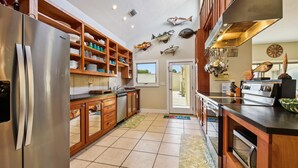 A kitchen with wooden cabinets, stainless steel appliances, and decorative fish on the wall. - Welcome to Sunset Sails & Wagging Tails! (St. George Island)