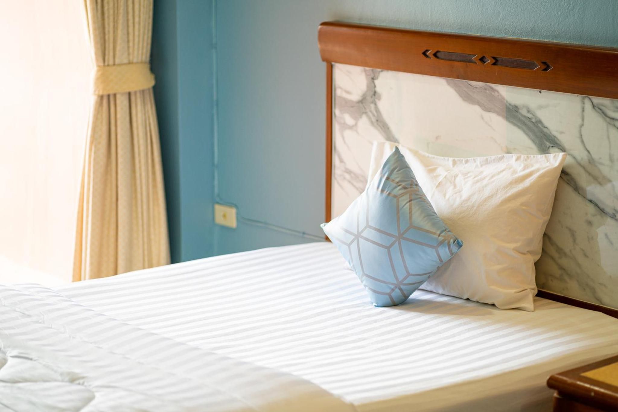 Una cama bien hecha con cabecera de mármol, dos almohadas y una mesita de noche de madera.