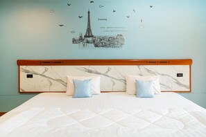 A hotel room with a marble headboard, two pillows, a bed, and a wall decal of a cityscape with birds. - Mayfa Hotel (Phuket)