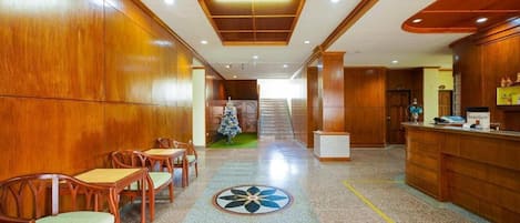 Un vestíbulo de hotel con paneles de madera, una recepción y una escalera que sube a otro piso.