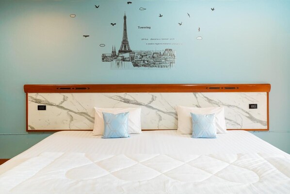 A hotel room with a marble headboard, two pillows, a bed, and a wall decal of a cityscape with birds. - Mayfa Hotel (Phuket)