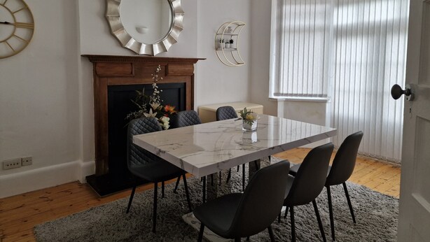 Un comedor con una mesa de mármol, sillas negras, una chimenea, un espejo grande y una araña.