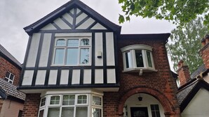 Una casa de estilo Tudor de dos pisos con fachada blanca y negra, detalles de ladrillo y un ventanal saliente.
