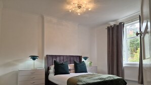Un dormitorio con cama, mesitas de noche, lámpara, ventana con cortinas y candelabro.