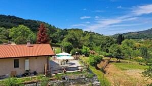 Ein Haus mit rotem Ziegeldach, einer Terrasse mit Gartenmöbeln und Blick auf einen Weinberg und Hügel im Hintergrund.