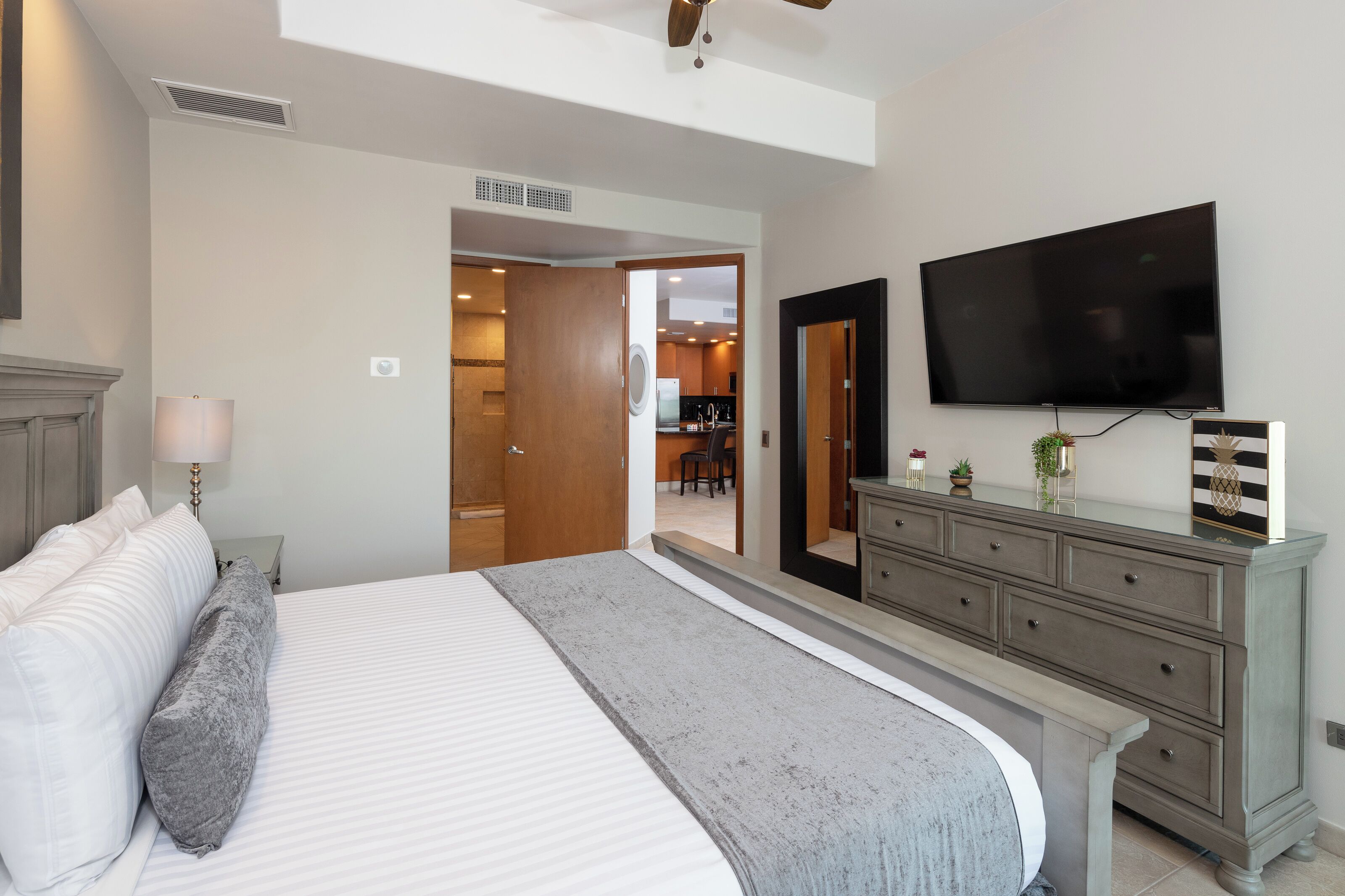 Un dormitorio con una cama grande, un aparador, un televisor y una puerta que da a una cocina.