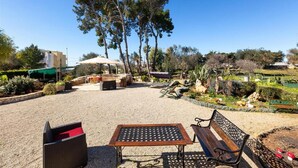 Un espace extérieur aménagé en patio, avec une table et des bancs, entouré d’arbres et d’un jardin.