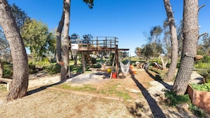Une terrasse en bois avec un hamac et un espace salon extérieur, le tout entouré d’arbres.