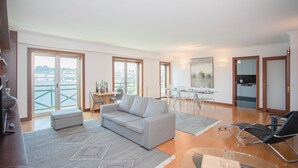 A spacious living area with a grey sofa, a black lounge chair, and a dining table with chairs. - Liiiving - Douro Riverside Apartment (Gondomar)