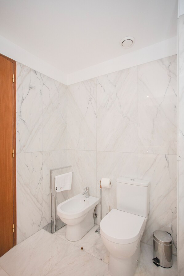 A bathroom with a toilet, bidet, and a trash bin. - Liiiving - Douro Riverside Apartment (Gondomar)