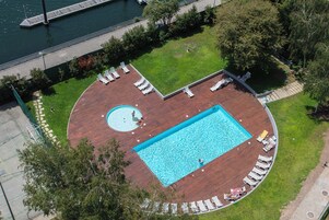 Vista aérea de una zona de piscina en la azotea, con una piscina rectangular, rodeada de sillones de descanso y un jacuzzi circular.