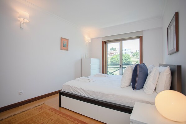 A modern bedroom with a large bed, a window with a view, and a bedside table.