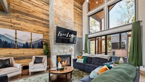 Una sala de estar acogedora con chimenea, ventanas amplias y un cartel de 'Treeline Vacation Rentals'.