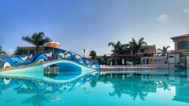 Ein Schwimmbecken mit einer Zierbrücke und Palmen im Hintergrund.