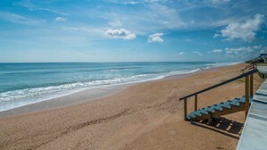 Una playa con una escalera que baja hasta la orilla, con vista al océano.