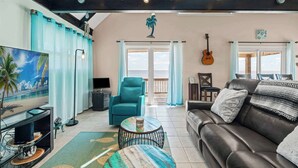 Un salón espacioso con un ventanal grande, un sillón azul verdoso, un sofá de cuero y una guitarra en la pared.