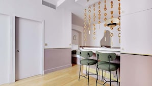 A modern kitchen with a bar area, two bar stools, and a decorative wall with hanging ornaments. - A Stunning Studio-Loft in Place Vendôme - Louvre (Paris)
