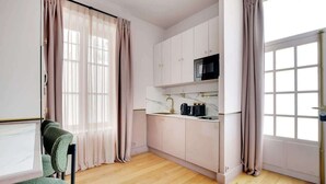 A modern kitchen with white cabinets, a black microwave, and a marble countertop. - A Stunning Studio-Loft in Place Vendôme - Louvre (Paris)