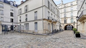 A cobblestone courtyard with buildings on either side, featuring a central archway and a bicycle parked near the entrance. - A Stunning Studio-Loft in Place Vendôme - Louvre (Paris)