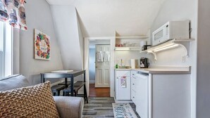 A compact kitchen with white cabinets, a microwave, and a coffee maker. There is a small dining area with a table and chairs, and a patterned rug on the floor. - Beautiful inn, Lighthouse Landing. #5 Beach Rose (Ogunquit)