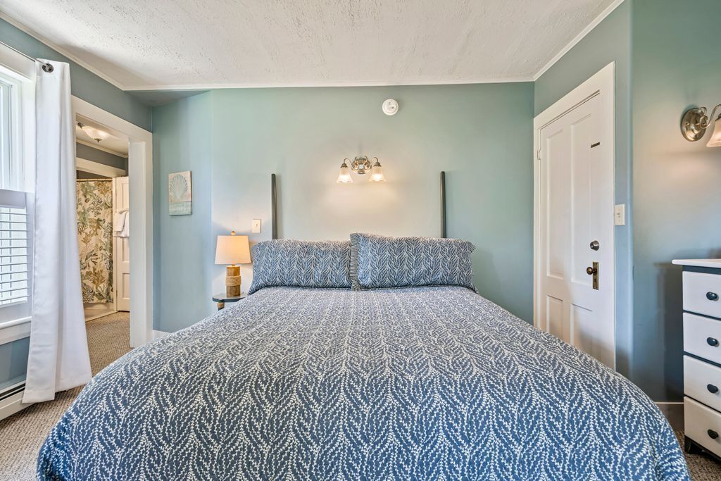 A bedroom with a large bed, a nightstand, a lamp, and a door.