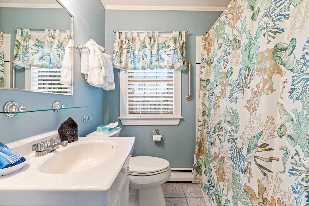 Un baño con lavamanos, inodoro y ventana con persianas.