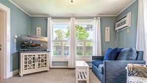 A living room with a blue couch, a white cabinet, and a painting of a lighthouse. - Beautiful inn, Lighthouse Landing. #2 Sea Cliffs (Ogunquit)