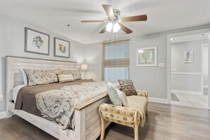 A bedroom with a bed, a chair, a ceiling fan, and artwork on the walls.