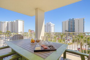 A balcony with a table set for dining, featuring a cheese board, salmon, and fruit.