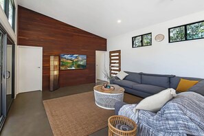 Een moderne woonkamer met een houten accentmuur, een grijze bank, een ronde salontafel en een grote flatscreen televisie aan de muur bevestigd.