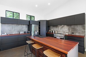 Een moderne keuken met donkere kastjes, een centraal kookeiland met krukken, een ingebouwde kookplaat en grote ramen.