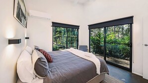 Quarto moderno com uma cama grande, um ventilador de teto e vista para o verde através de amplas portas deslizantes.