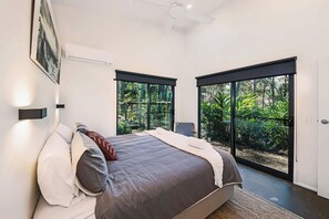 Een moderne slaapkamer met een groot bed, een plafondventilator en uitzicht op groen via grote schuifdeuren.
