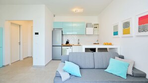 A modern kitchen with teal cabinets, a grey sofa with blue cushions, and a white countertop. - Hedera Estate, Hedera A35 (Dubrovnik)