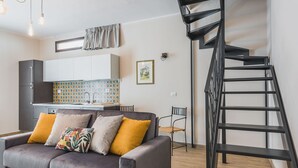 A modern living room with a sofa, a staircase, and a kitchen area. - Venuto Home by Wonderful Italy - Deep Blue (Catania)