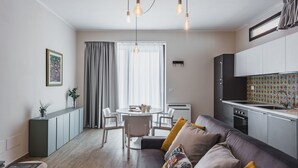 A modern living room with a sofa, a dining table, and a kitchen area with cabinets and a stove. - Venuto Home by Wonderful Italy - Deep Blue (Catania)