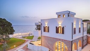Un edificio moderno con facciata in pietra, ampie finestre ad arco e vista sul mare.